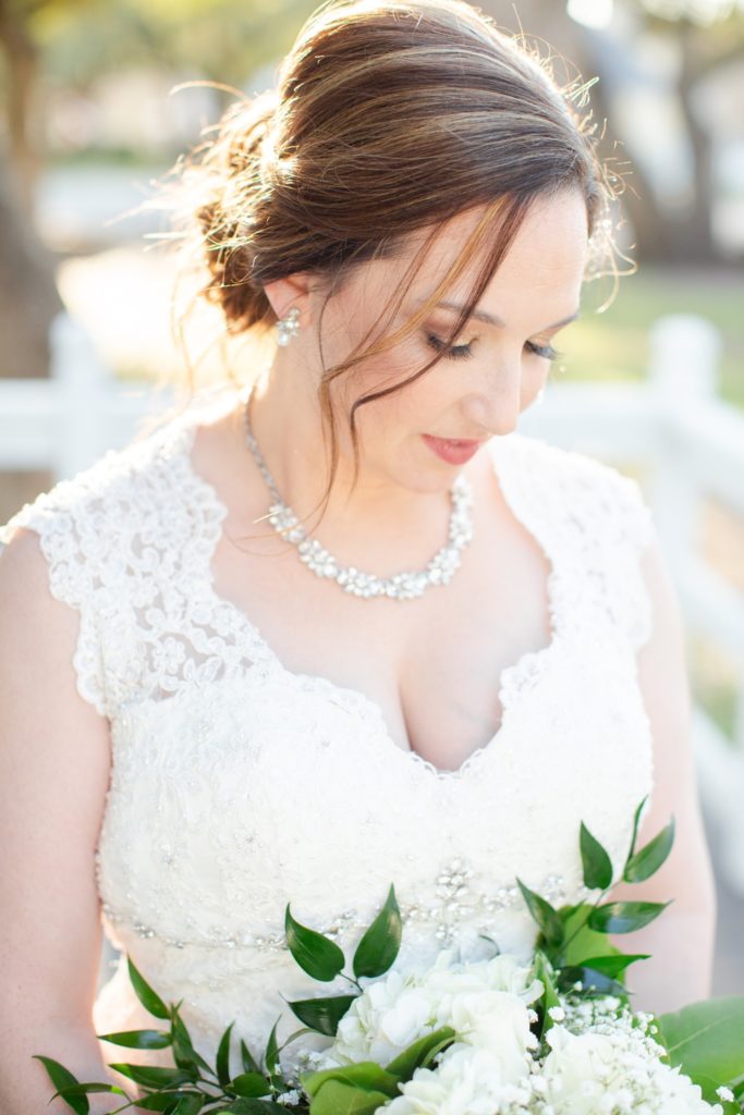 A bride gazes down on her white bouquet while the sun glows on her hair. 