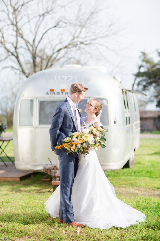 Smiling bride and groom hugging in front of their wedding airstream.