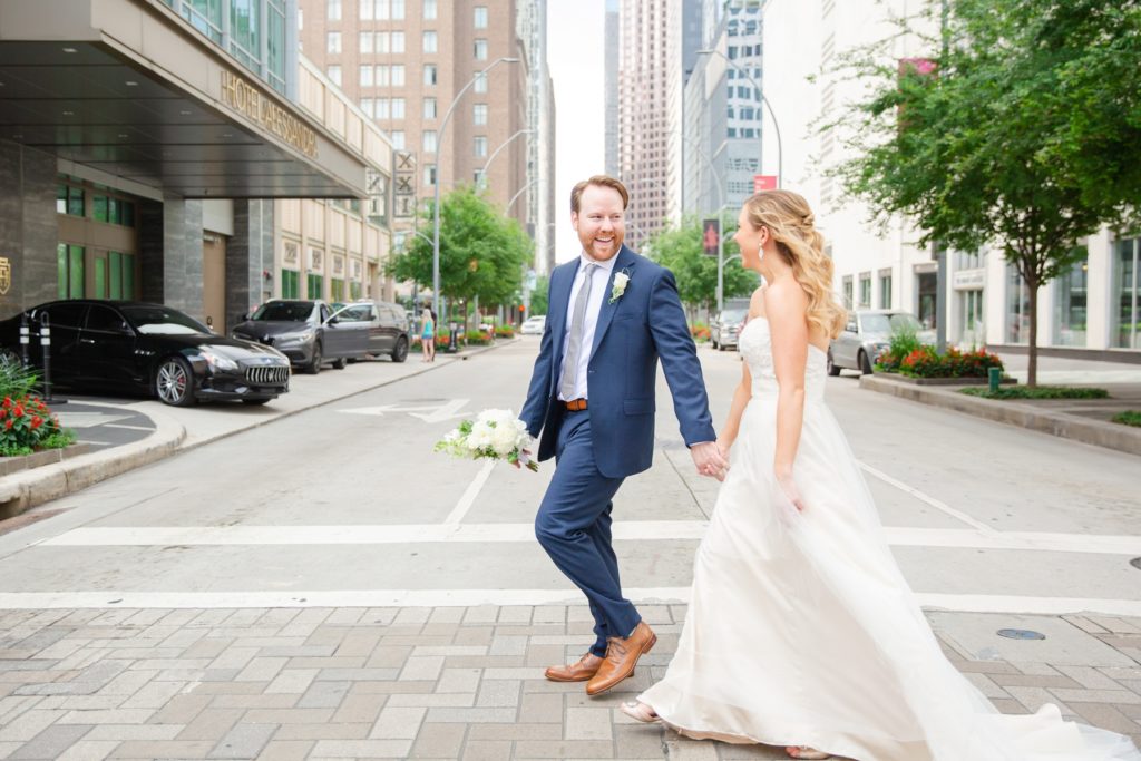 A bride and groom cross a busy street downtown.