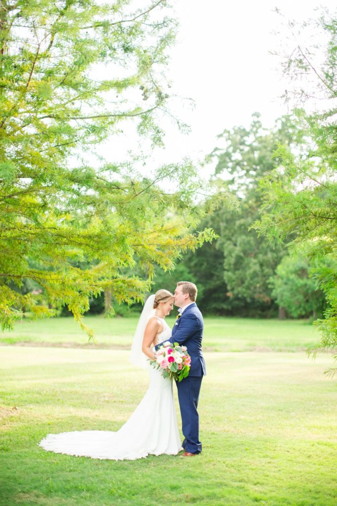A bride and groom hug under cypress trees in the summer.