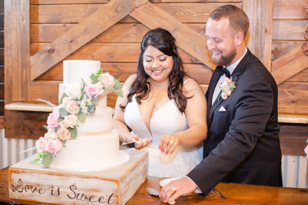 A bride and groom laugh as they cut their wedding cake. 