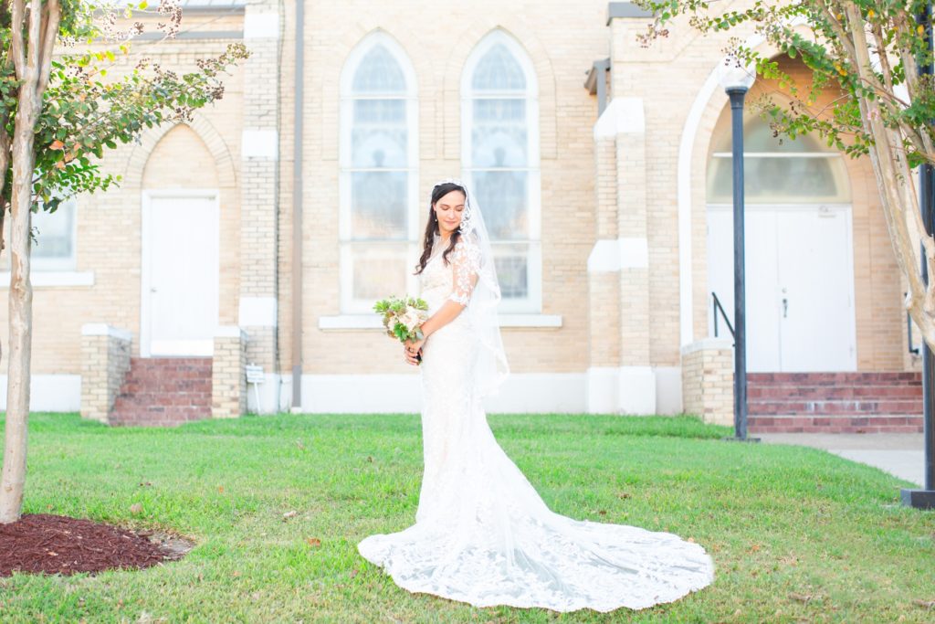 A bride poses dramatically in front of a stain glass catholic church.